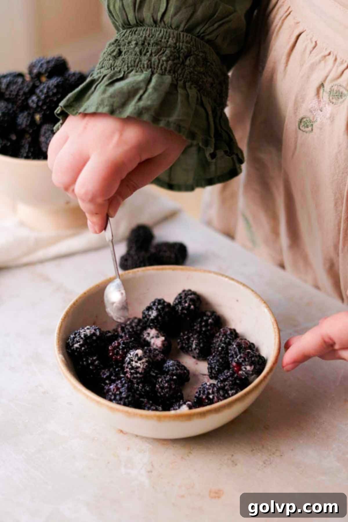 Coating fresh blackberries lightly with flour to prevent sinking in the muffin batter.