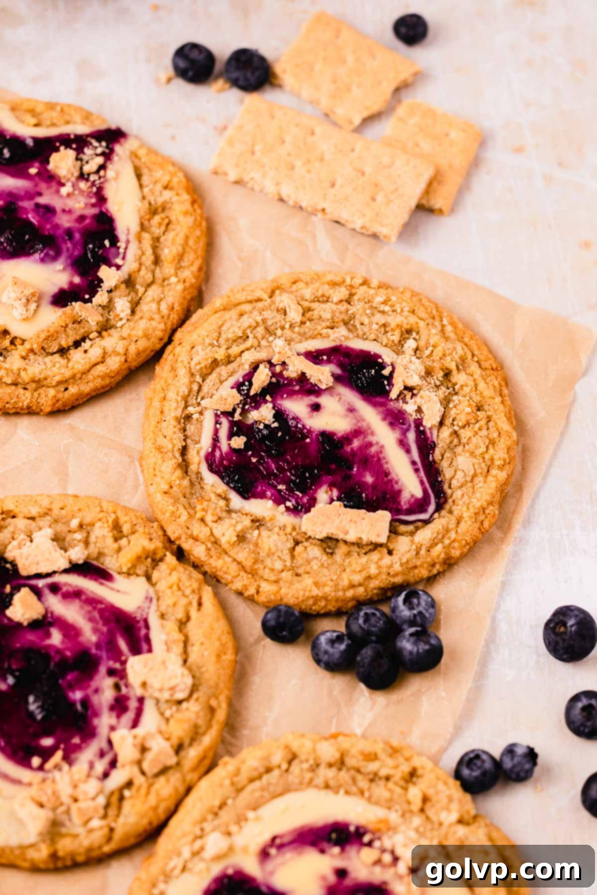 blueberry cheesecake cookies on parchment paper with fresh blueberries around