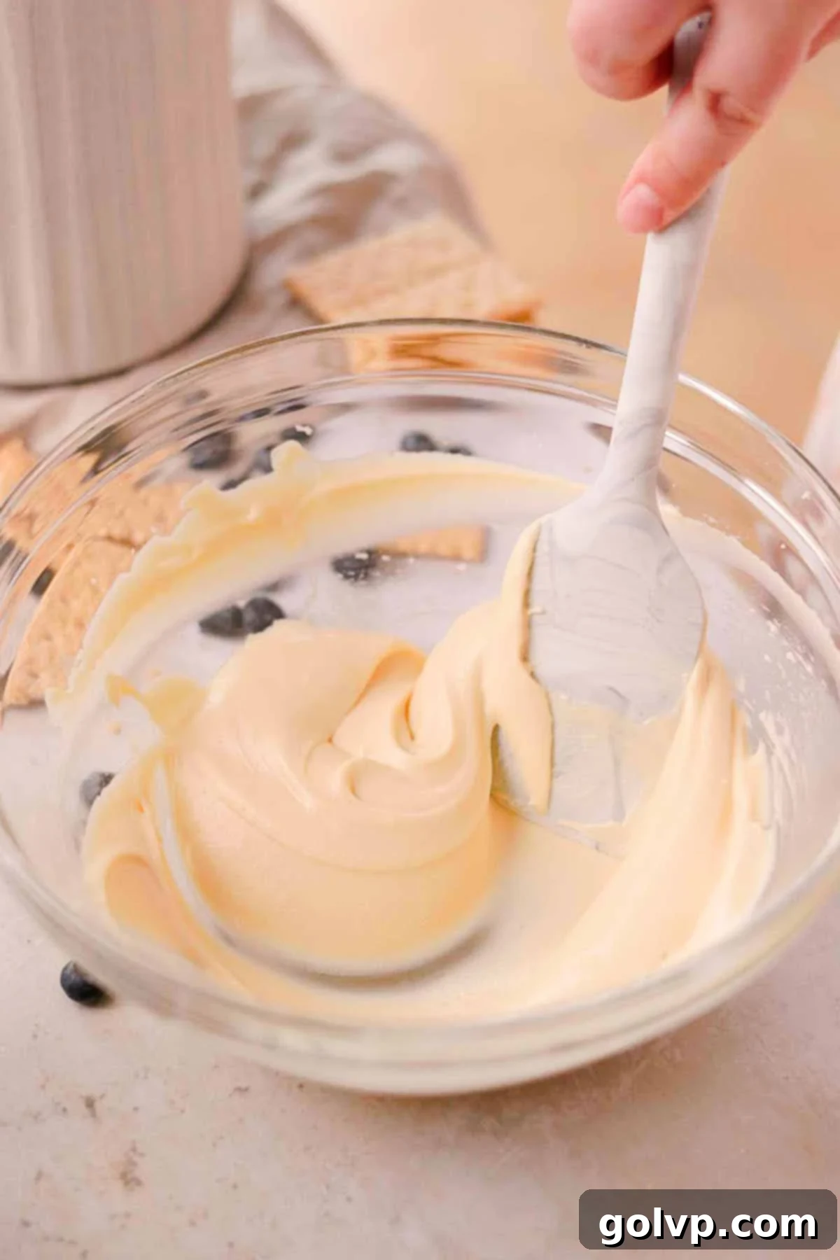 fold smooth cheesecake mixture in a glass bowl with a rubber spatula