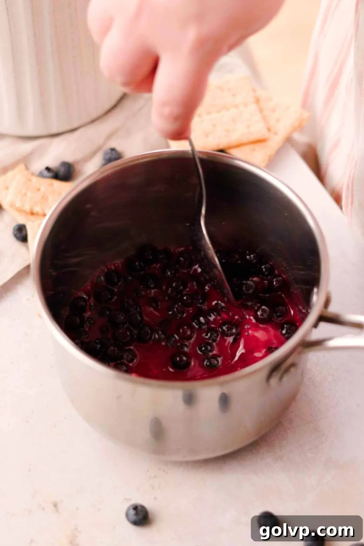 stirring blueberry sauce with a spoon in a small saucepan
