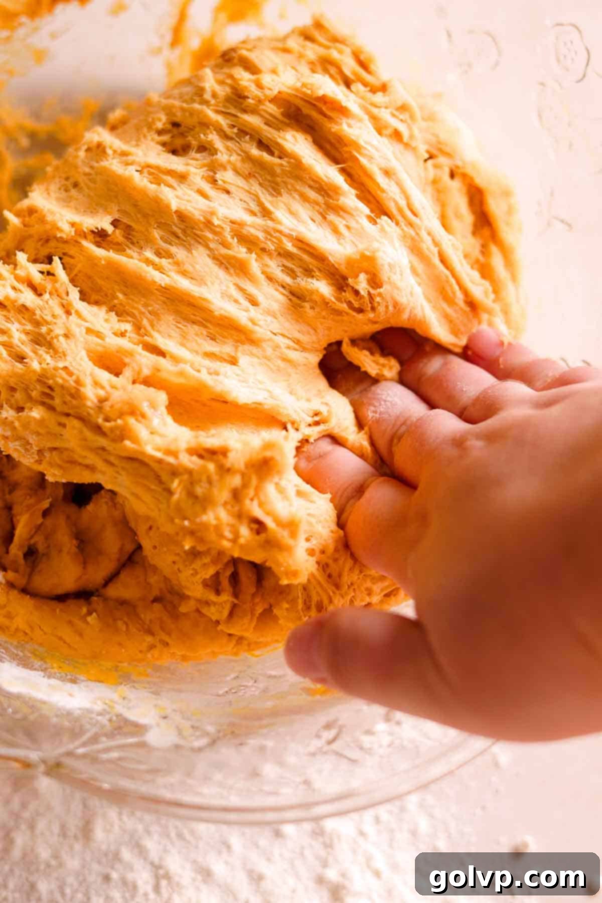 punching down the soft donut dough in a large glass bowl