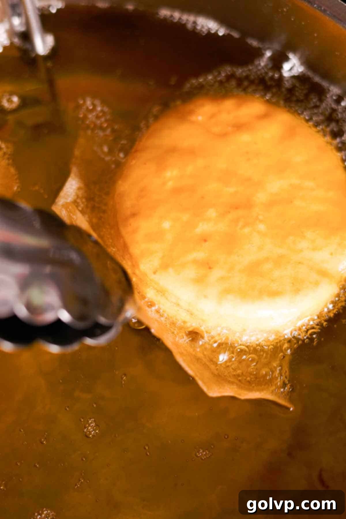 frying donut dough rounds in oil and removing parchment paper square with tongs