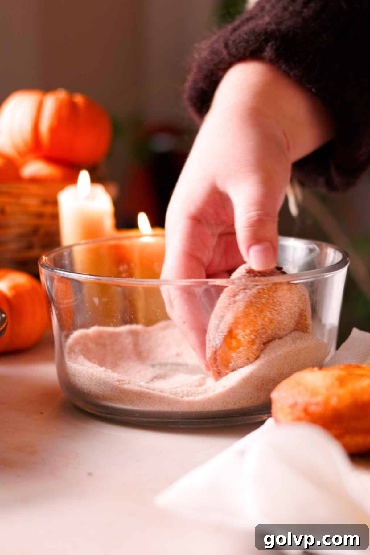 coating fried donuts with spiced sugar mixture in glass bowl