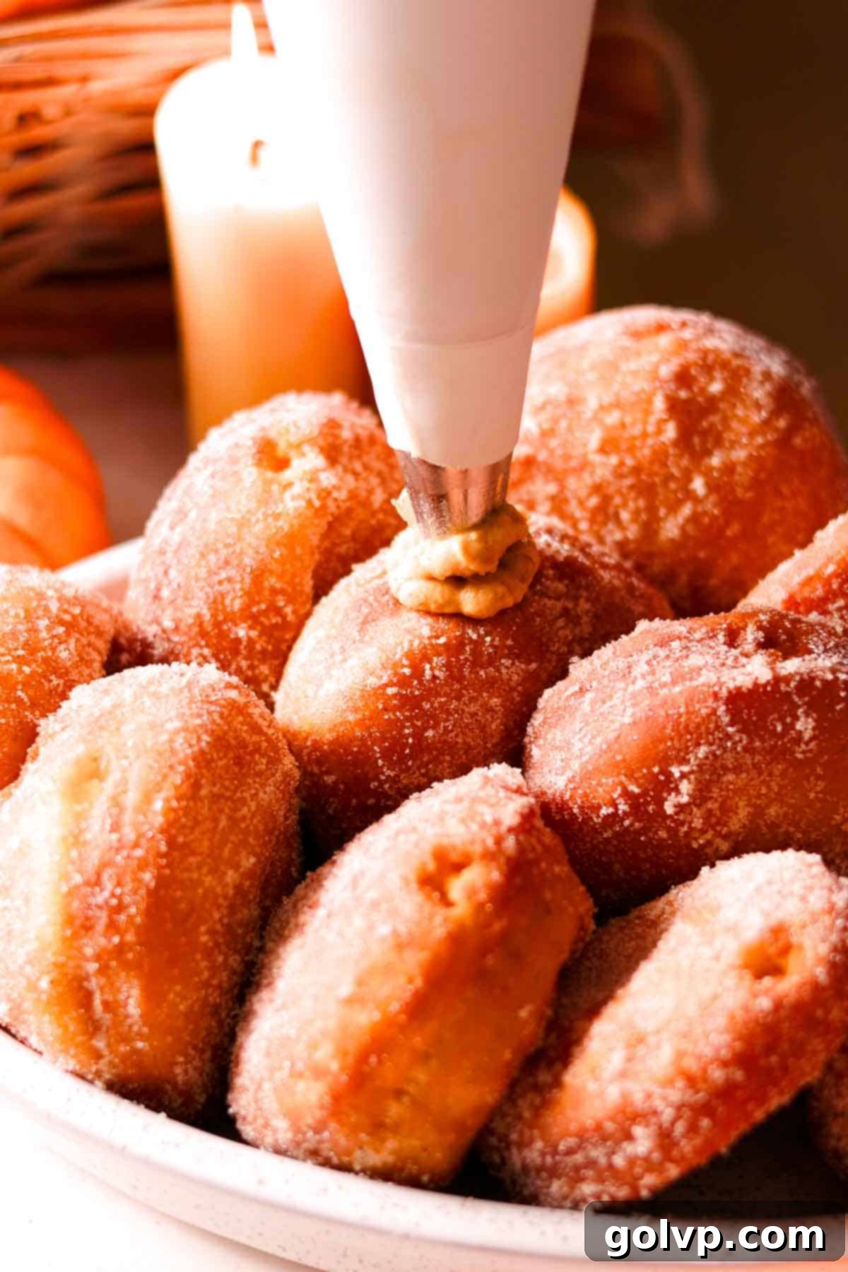 filling sugar coated donuts with cream using a white cloth pastry bag