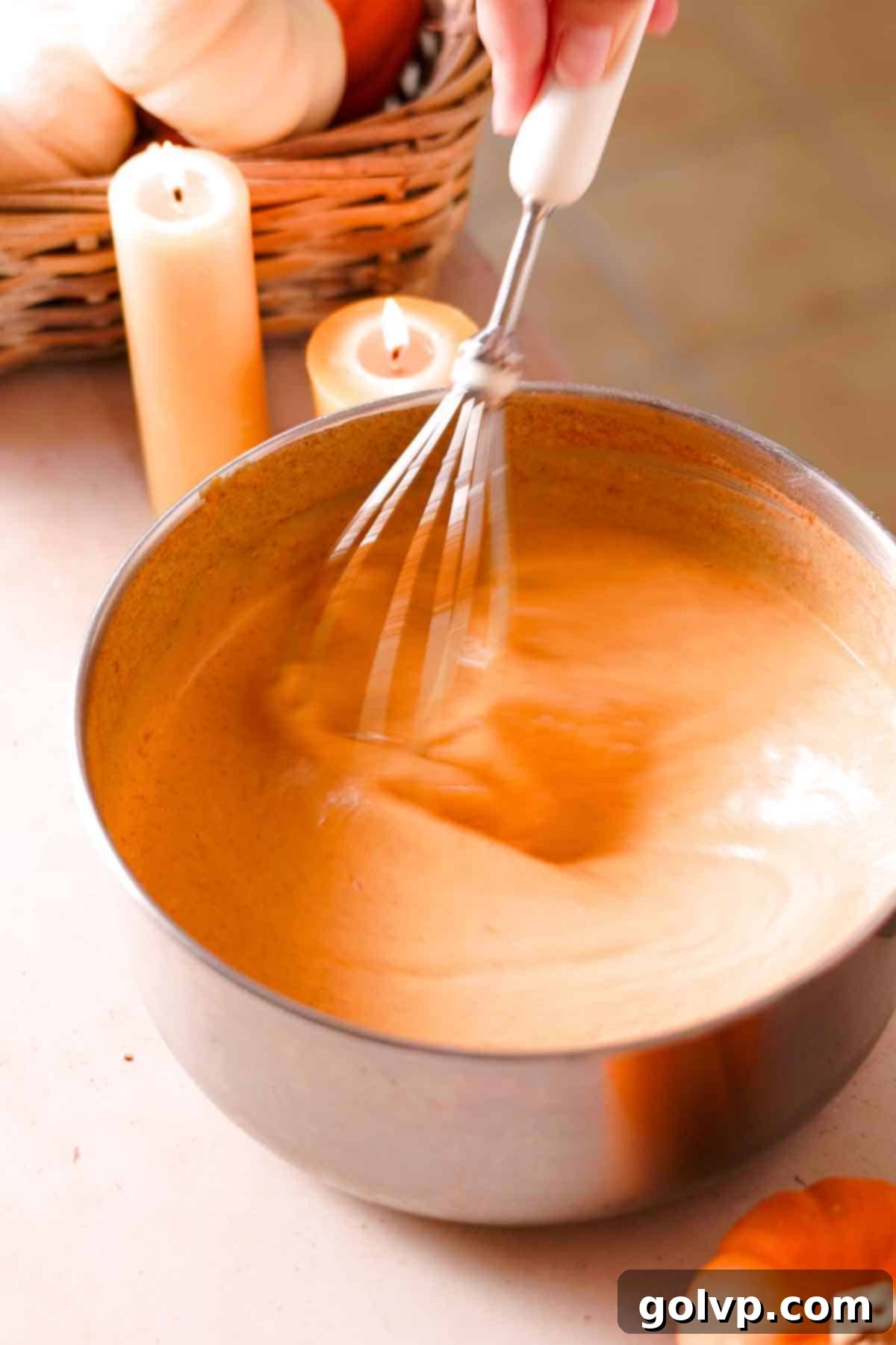 orange pumpkin custard in saucepan being whisked with candles in the background
