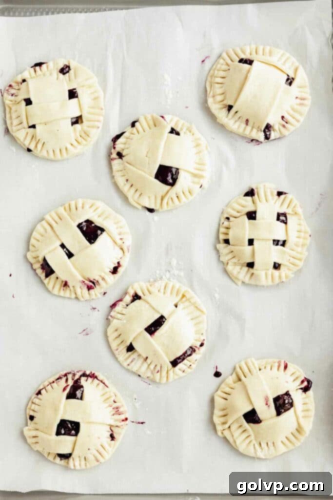 Mini blueberry pies on a baking tray, brushed with egg wash and ready for the oven.