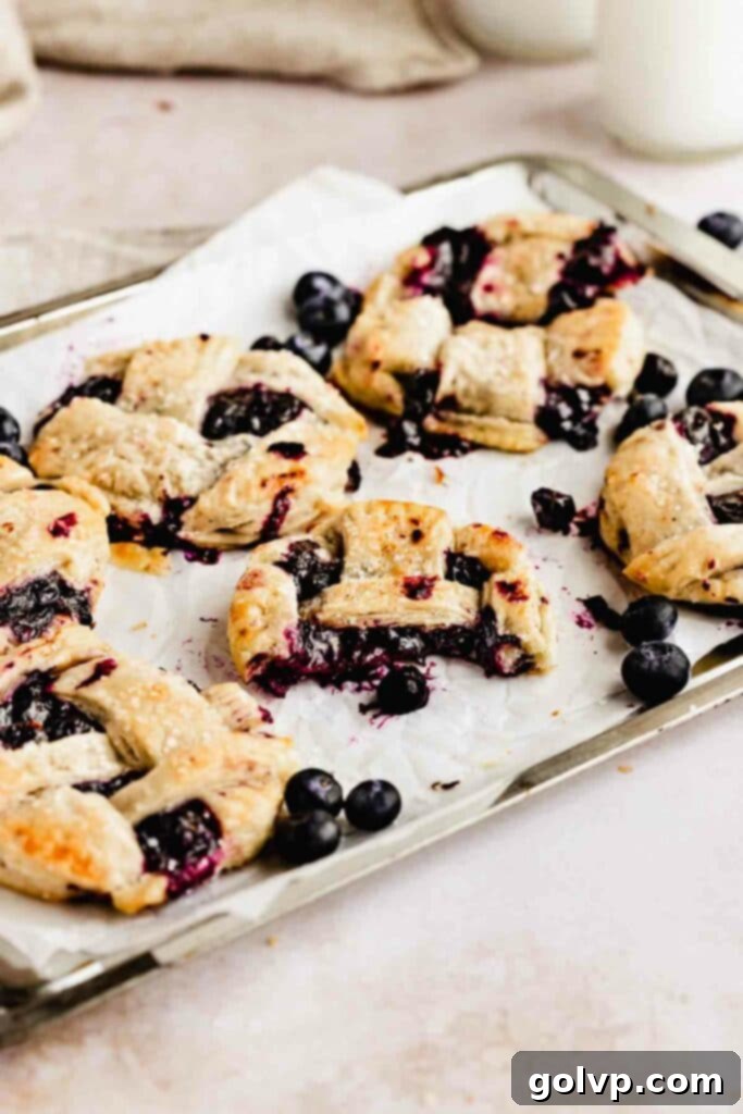 A half-eaten mini blueberry pie on a baking tray, showcasing its perfectly golden and flaky crust.