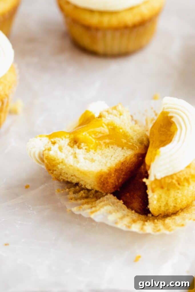 A mango cupcake beautifully cut open, revealing the abundant, jammy mango filling inside its fluffy vanilla cake.