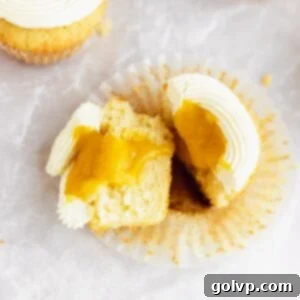 Cut open mango cupcake filled with runny mango filling, showing layers of fluffy cake, vibrant filling, and smooth condensed milk buttercream.