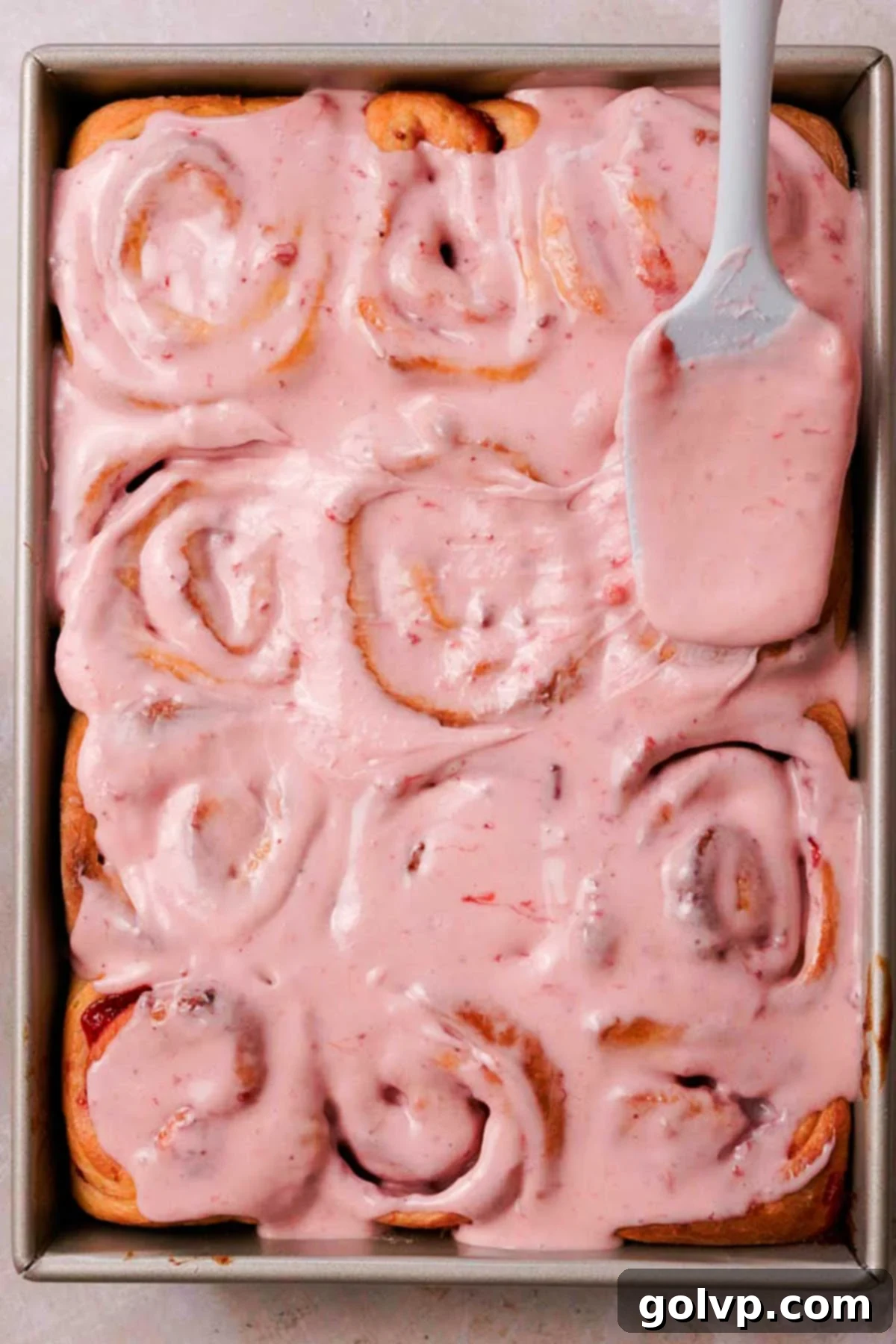 Fresh Strawberry Cinnamon Swirls 20 Spreading a thick layer of pink strawberry cream cheese glaze over warm, baked strawberry cinnamon rolls in a pan.