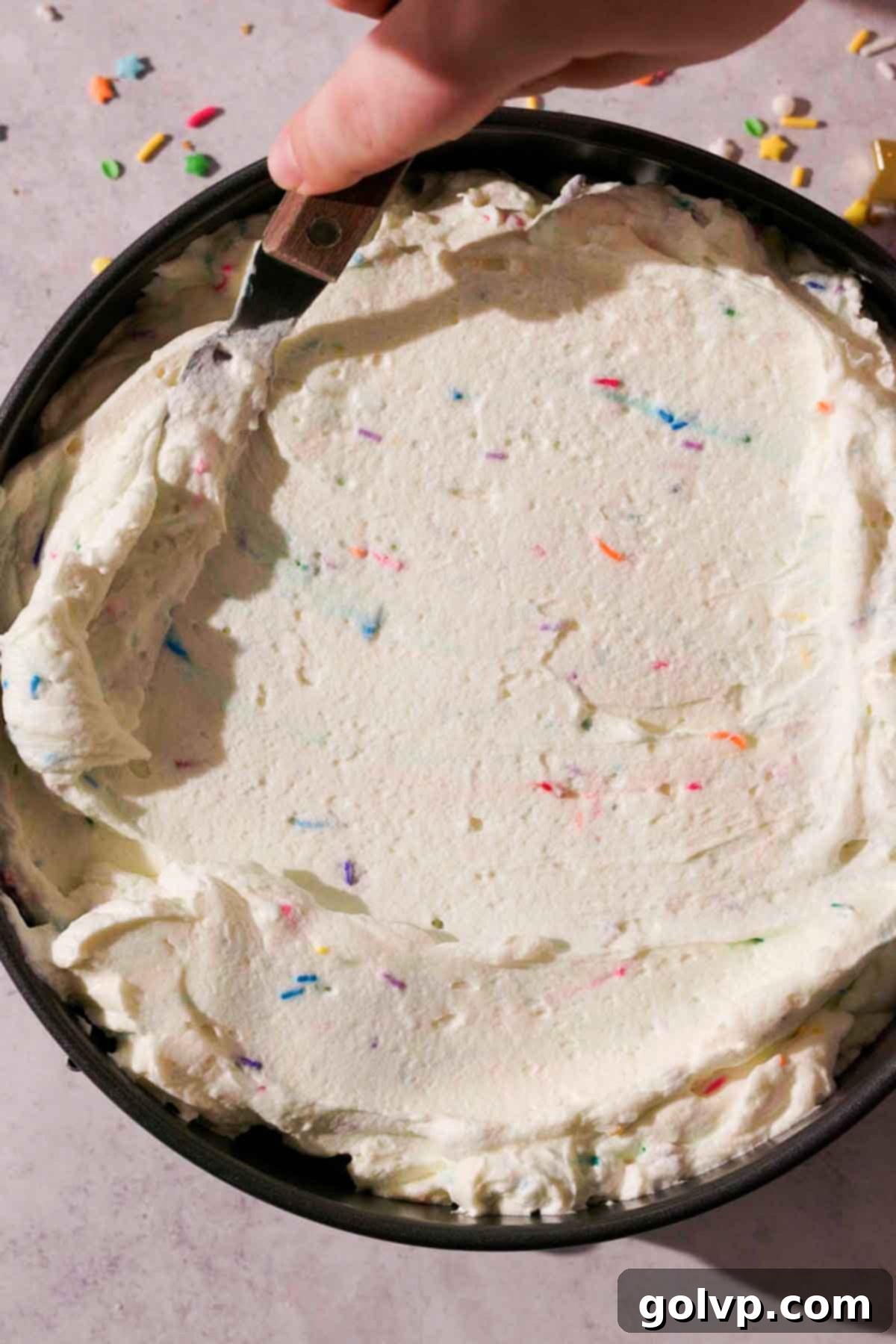 using a small offset spatula to spread cheesecake filling on top of crust in baking pan