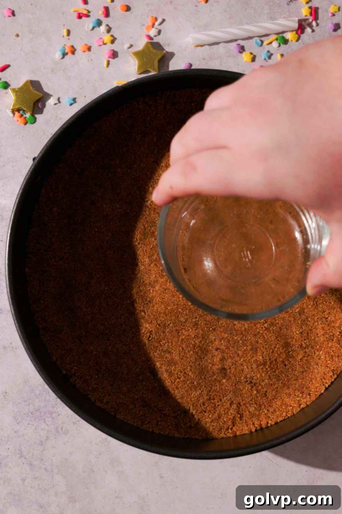 pressing graham cracker crust into the bottom of cake pan using a glass container bottom