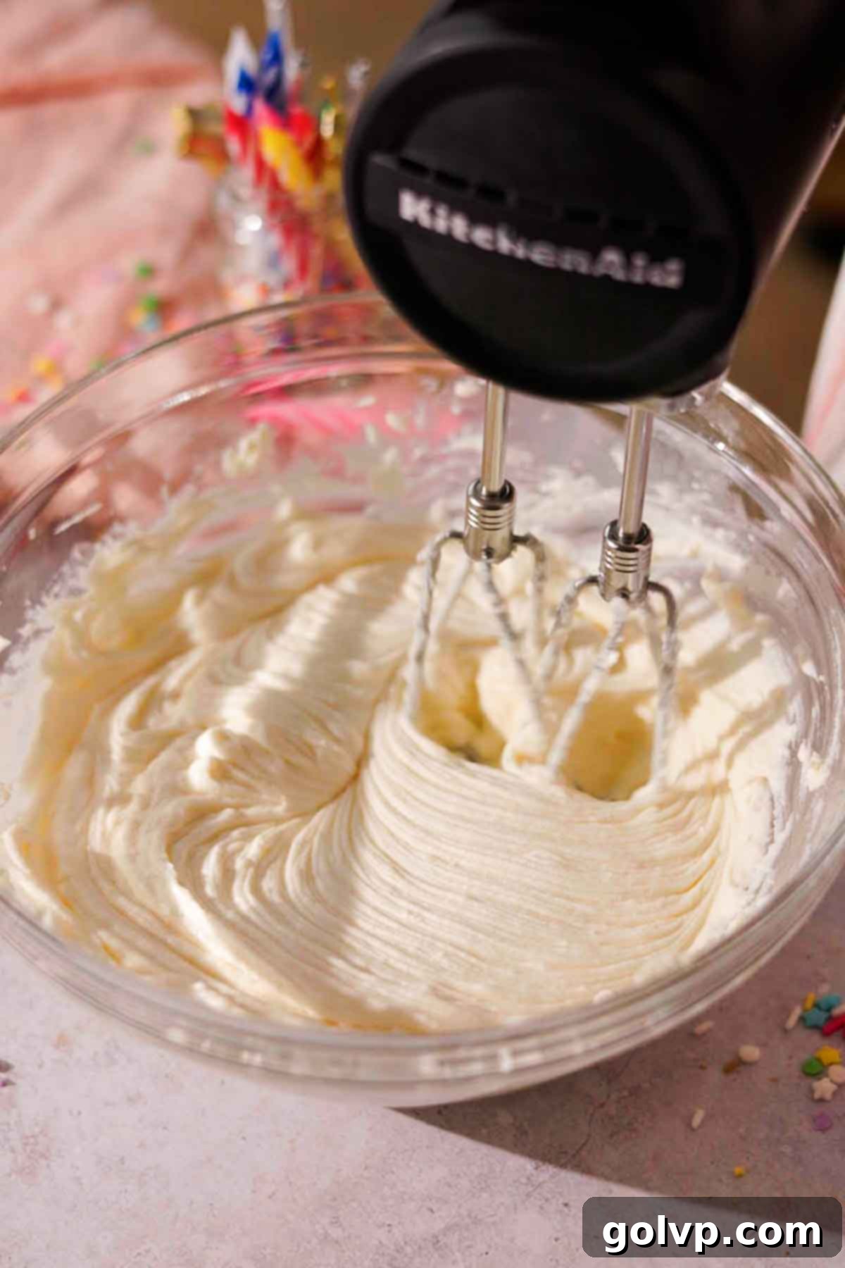 beating cream cheese with an electric mixer in a large glass bowl