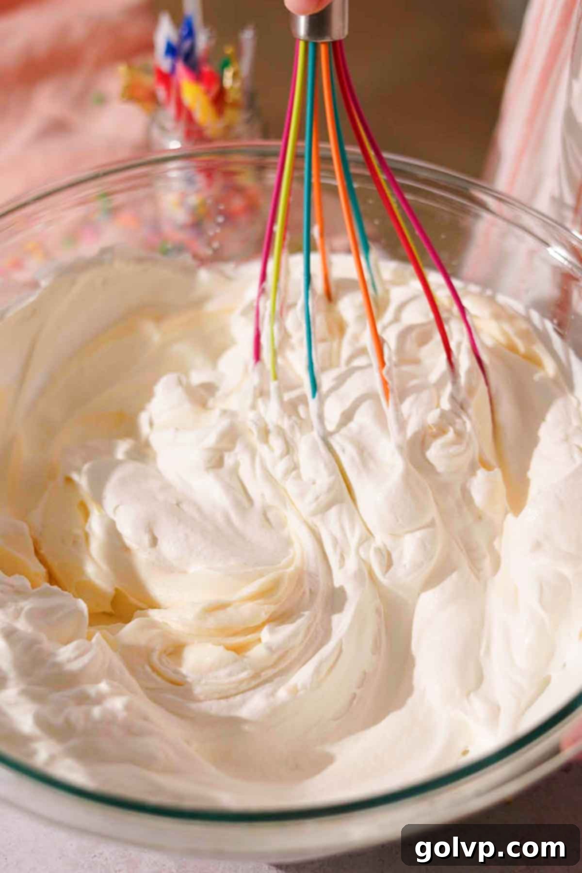 folding cheesecake filling ingredients with rainbow whisk in glass bowl