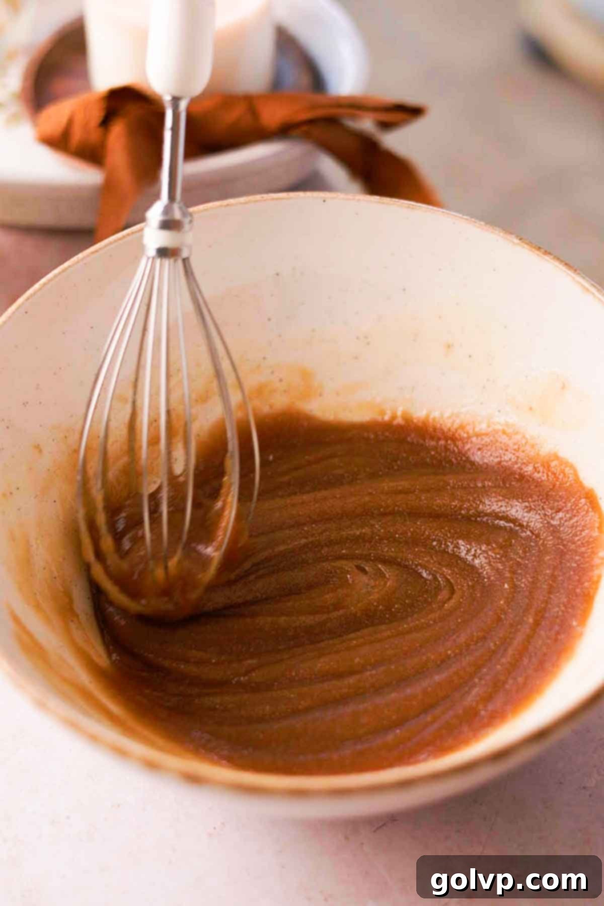 whisking melted butter and sugar inside ceramic bowl with wire whisk