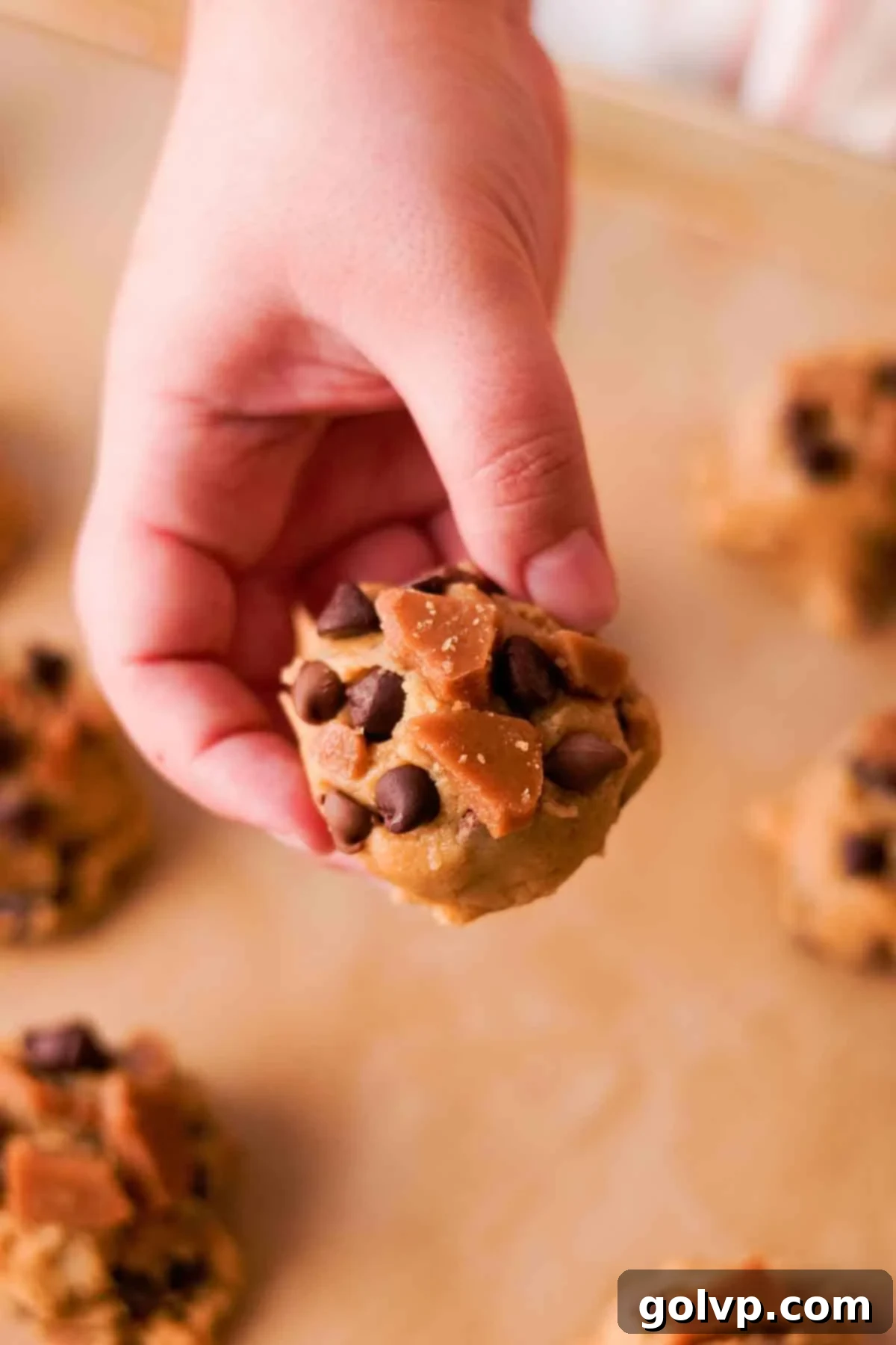 Heavenly Toffee Cookies: Our Foolproof Homemade Toffee Secret 17 holding scooped cookie dough ball topped with toffee and chocolate chips
