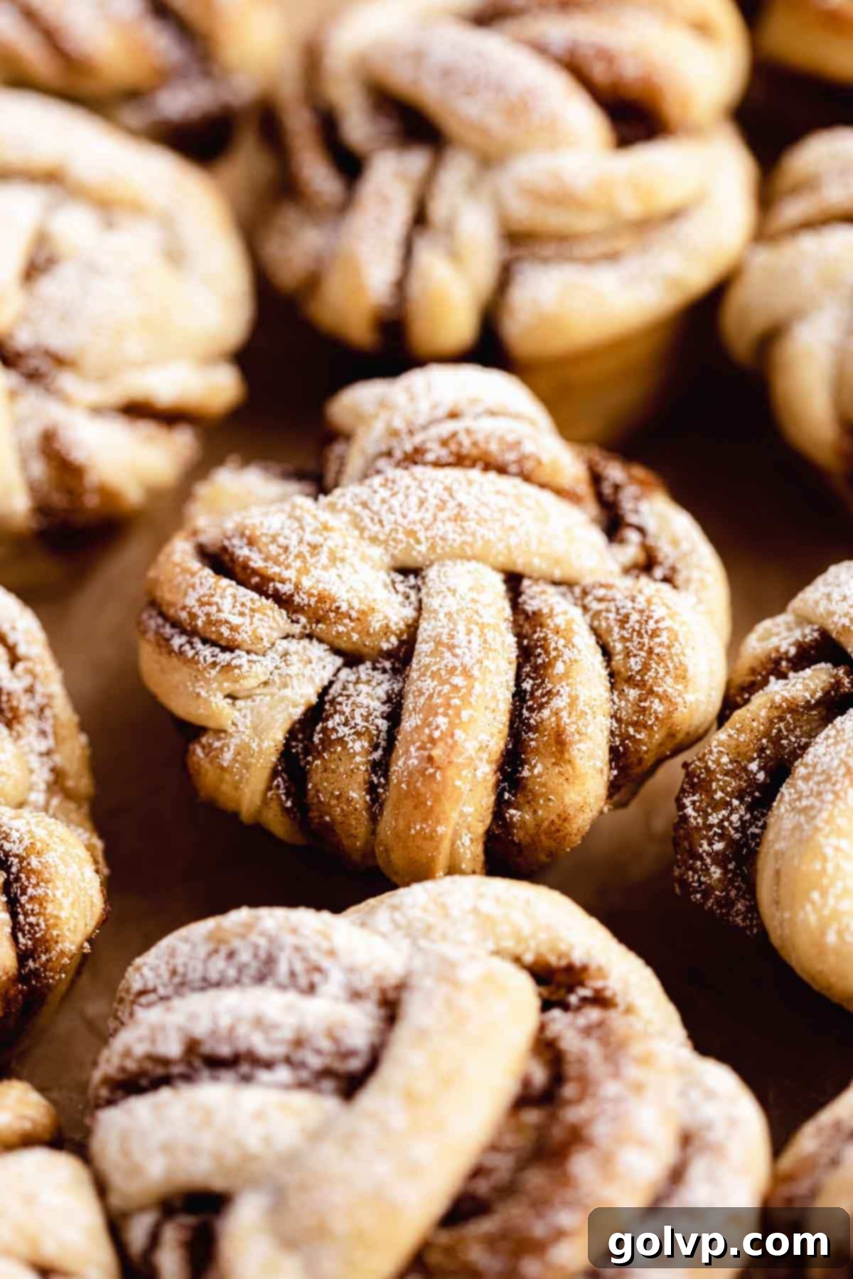 Cinnamon Swirl Delights 11 Baked twisted cinnamon rolls on parchment paper, dusted with icing sugar