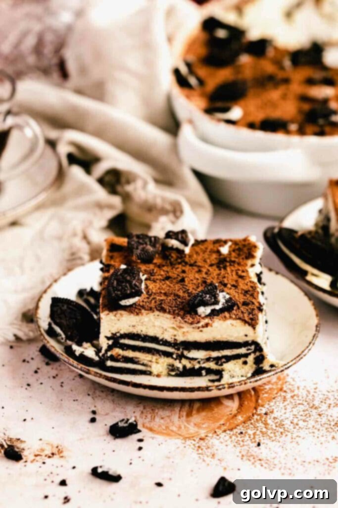Oreo Tiramisu Delight 4 A perfectly portioned slice of Oreo Tiramisu on a white plate, garnished with whole and crumbled Oreos, inviting indulgence.
