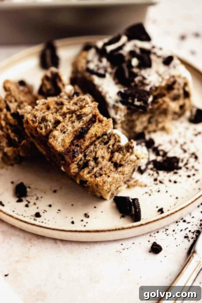 Decadent No-Knead Cookies and Cream Cinnamon Rolls 2 A single Cookies and Cream Cinnamon Roll on a plate, garnished with more crushed Oreos and a drizzle of cream cheese frosting.