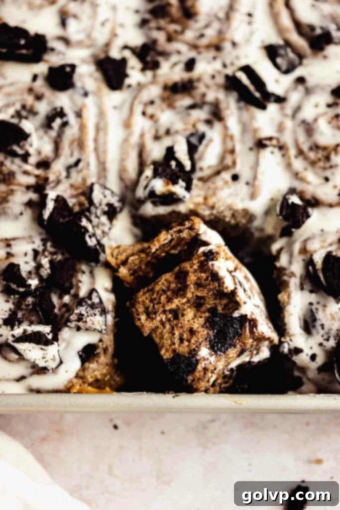 Decadent No-Knead Cookies and Cream Cinnamon Rolls 3 A close-up of a torn-apart cookies and cream cinnamon roll in a baking tray, showcasing its gooey center and fluffy texture.