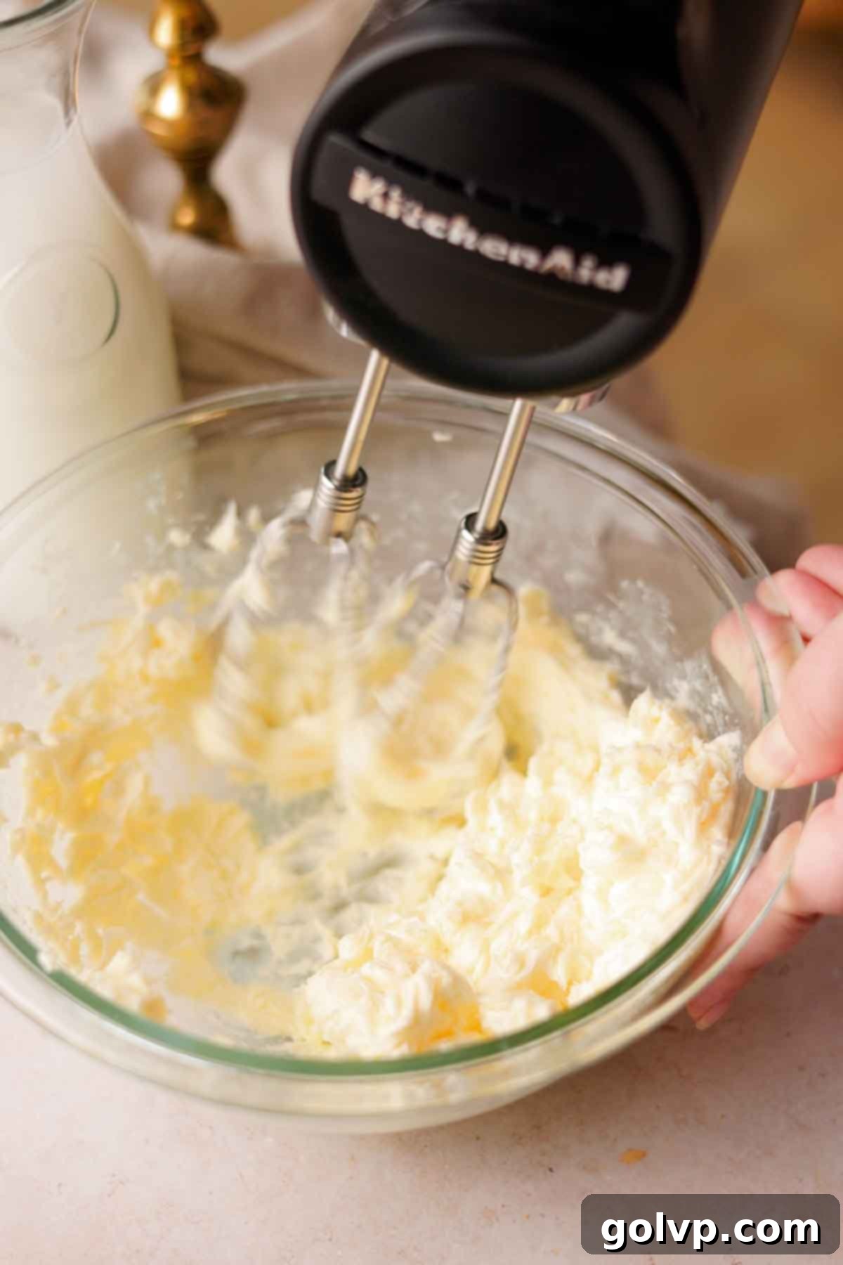 beating butter with a black electric handheld mixer in a glass bowl