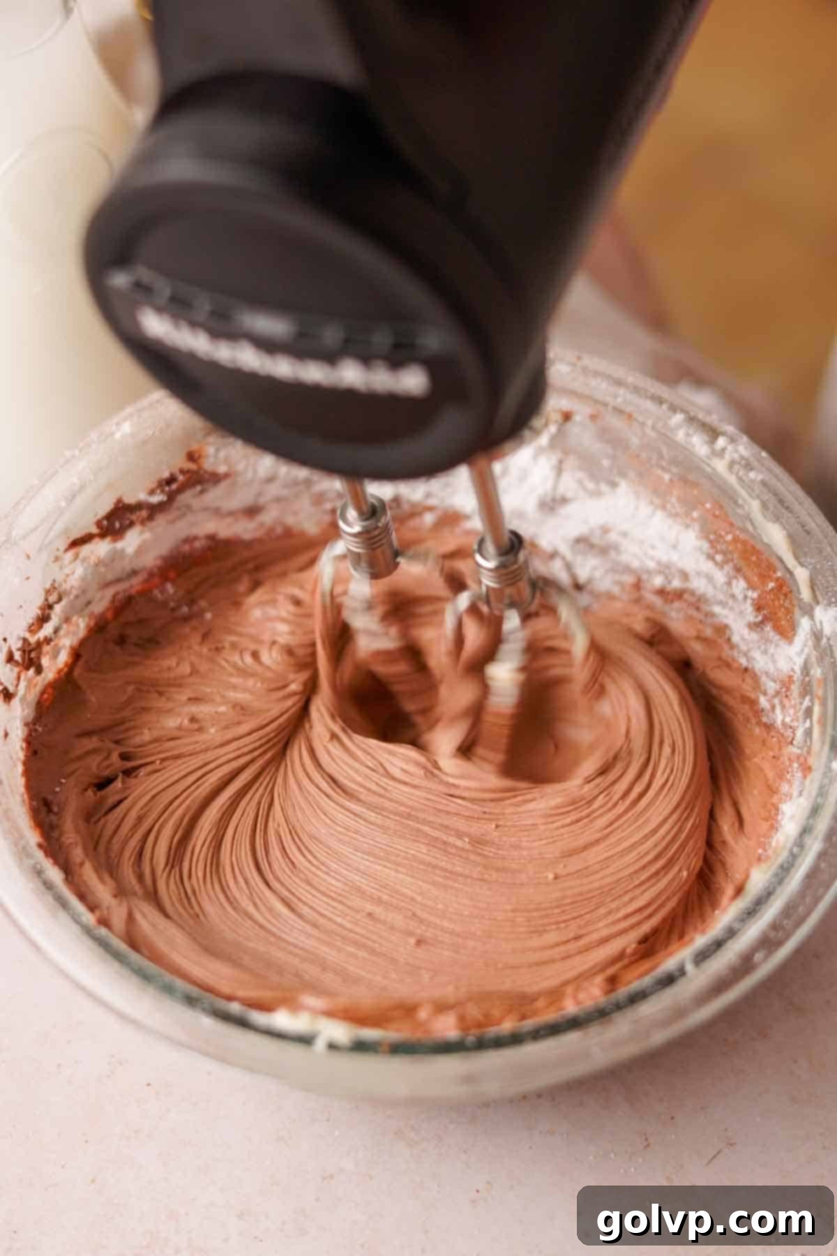 using an electric mixer to mix cocoa powder into nutella frosting