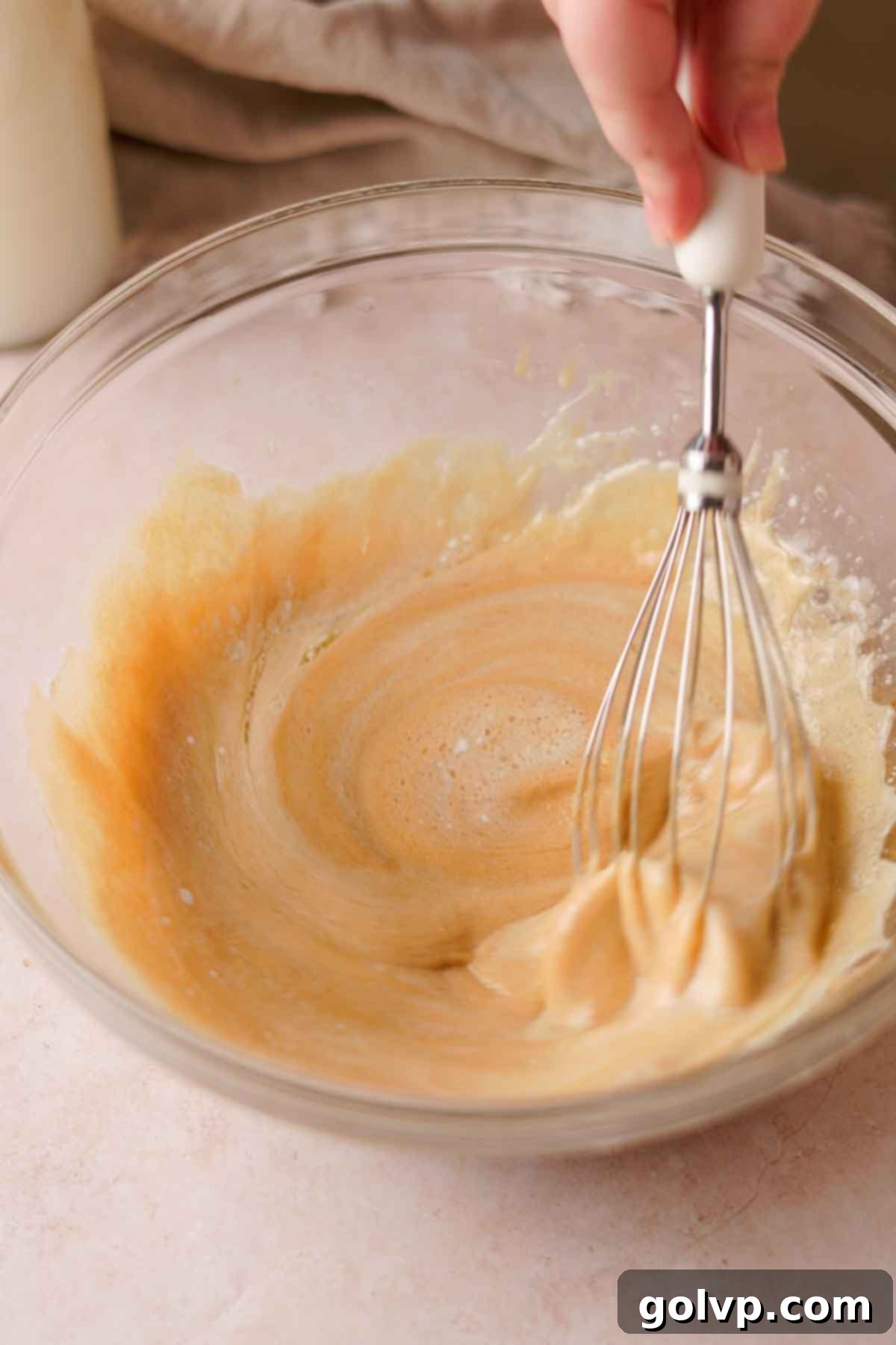 whisking wet ingredients for chocolate cupcakes in a glass bowl with a hand whisk