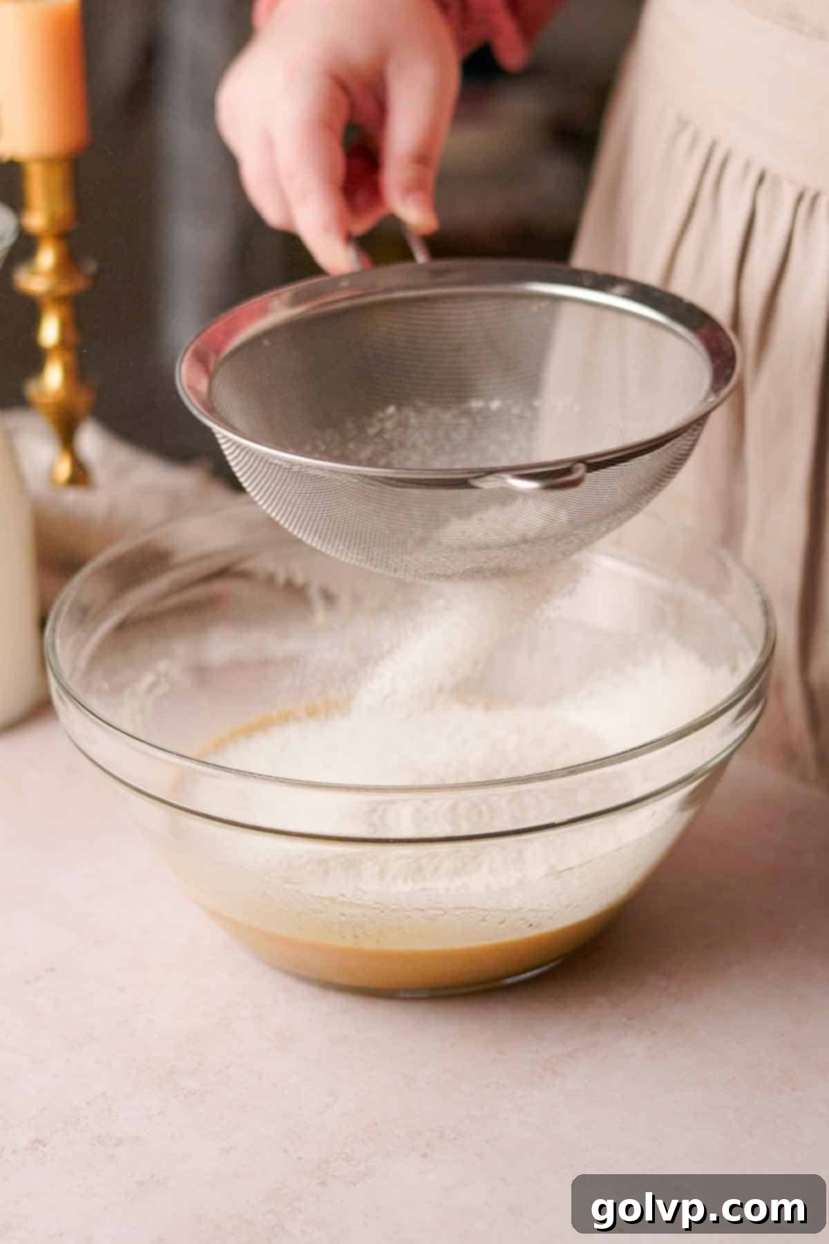 sifting flour into a large glass bowl with a wire sieve