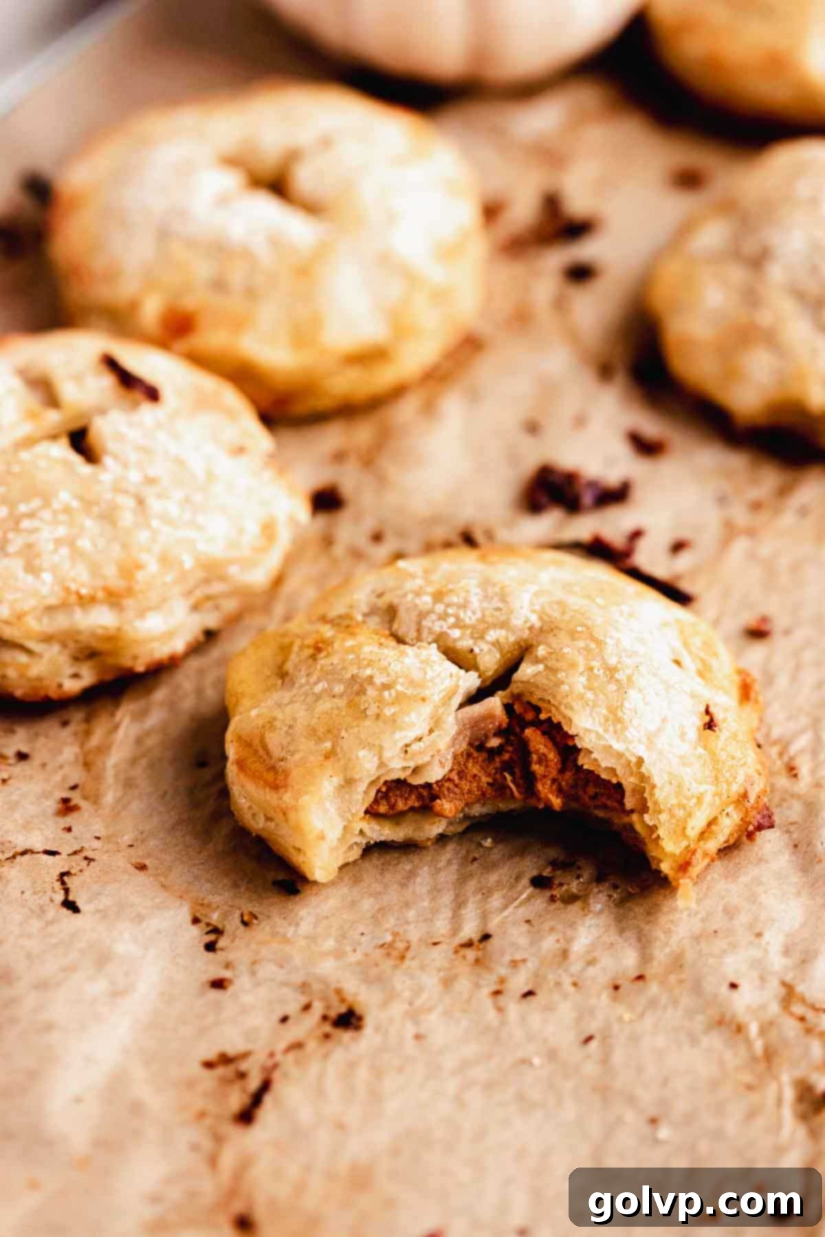 A close-up of a bitten hand pie, showcasing the flaky pastry and vibrant pumpkin filling.