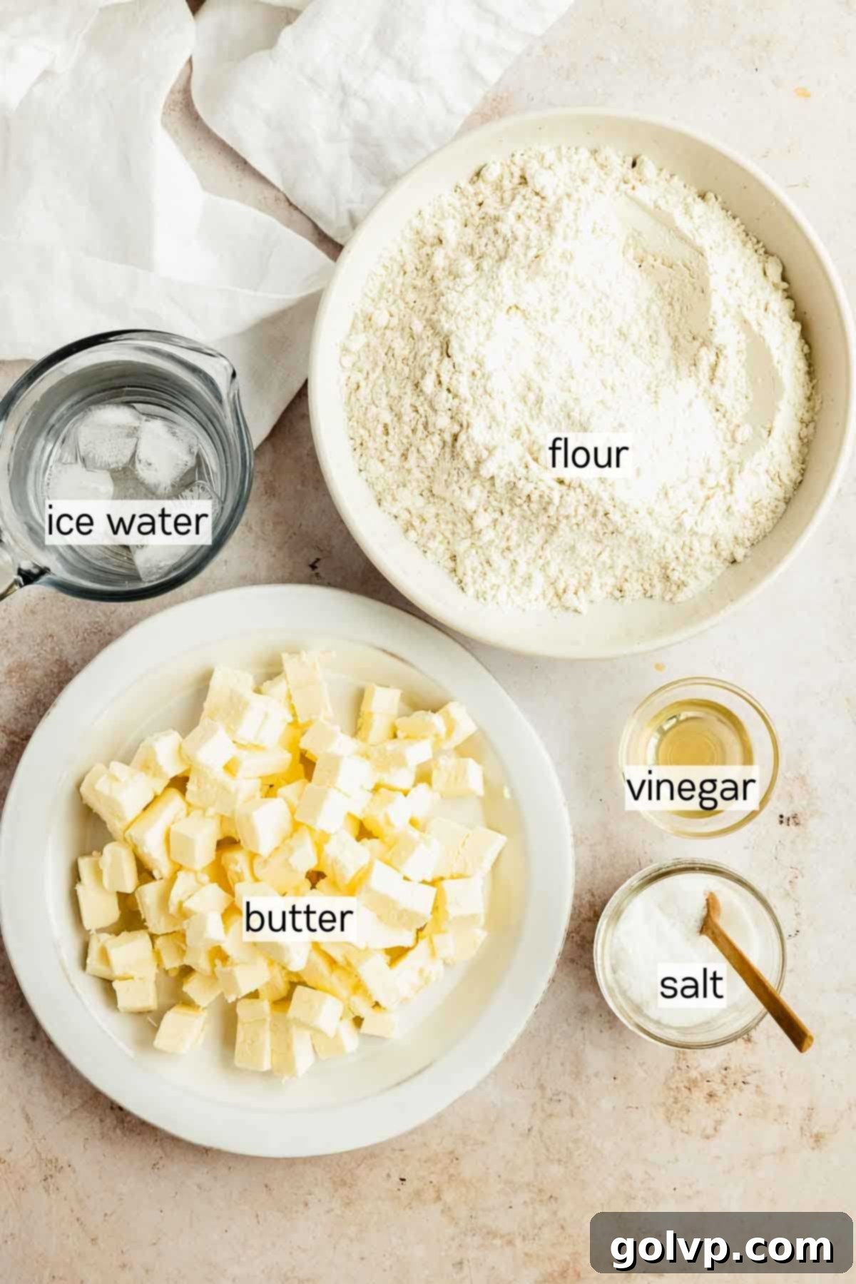 Bowls containing ingredients for pumpkin hand pie crust: flour, cubed butter, and a glass of water with vinegar.