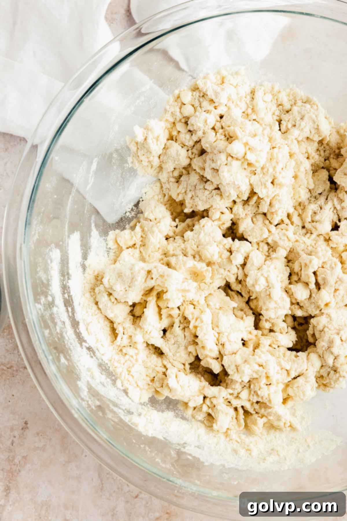 Shaggy pie dough beginning to come together in a mixing bowl.