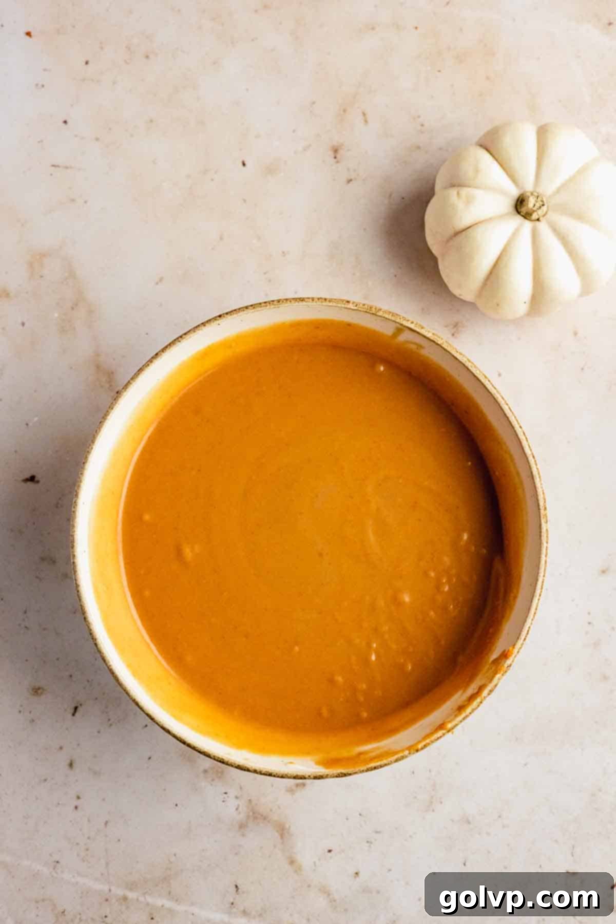 Close-up of pumpkin puree, buttermilk, and sour cream added to the wet ingredients, showing a smooth, creamy texture before dry ingredients are incorporated