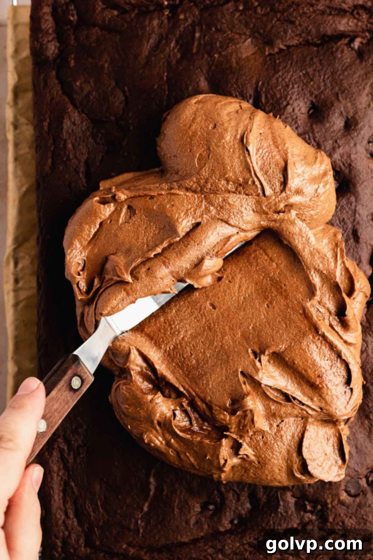 Smoothly spreading the dark, rich chocolate pumpkin frosting evenly over the top of the cooled sheet cake