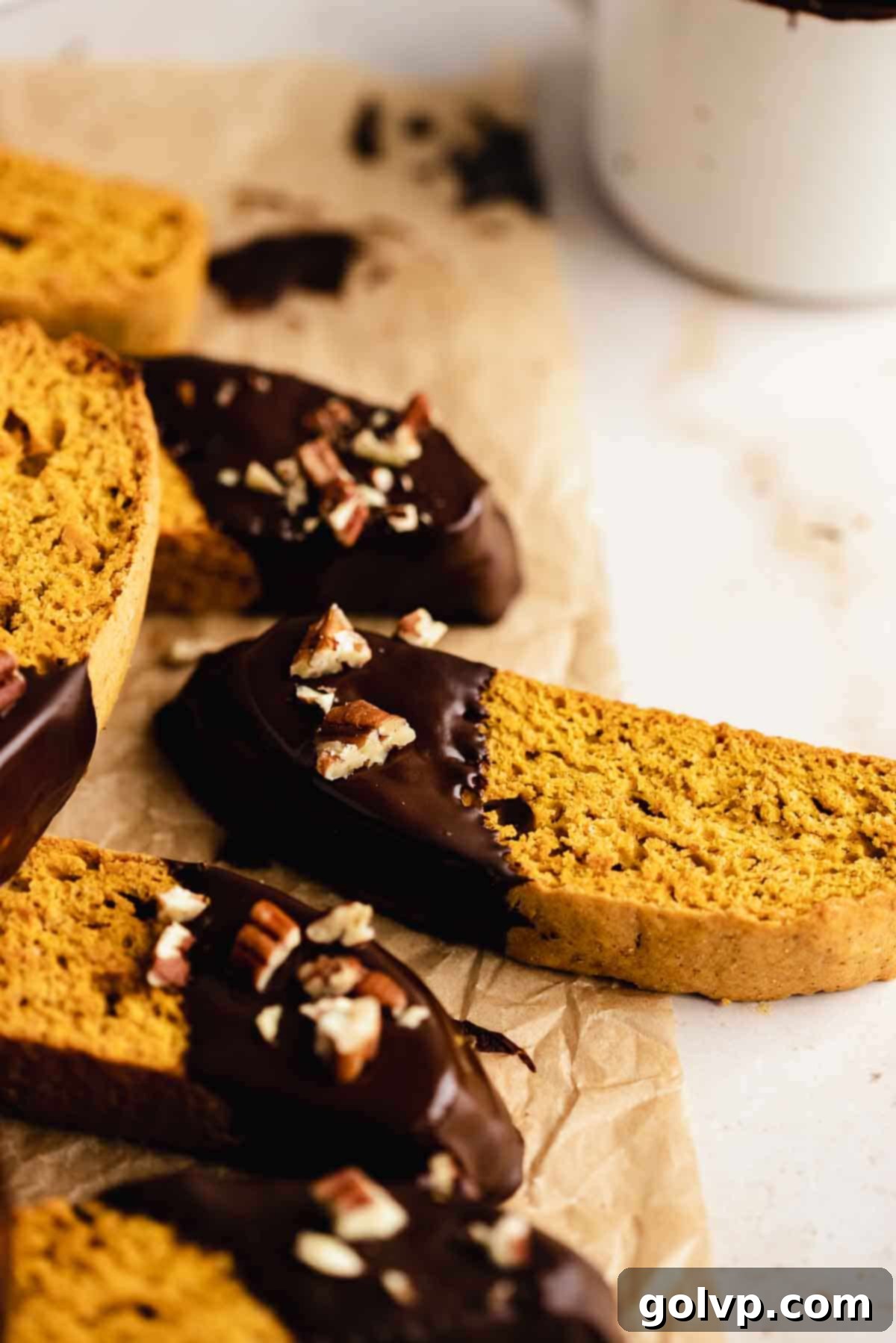 Autumn Pumpkin Biscotti 10 Freshly chocolate-dipped pumpkin biscotti laid out on parchment paper, some still glistening with melted chocolate and others adorned with chopped nuts.