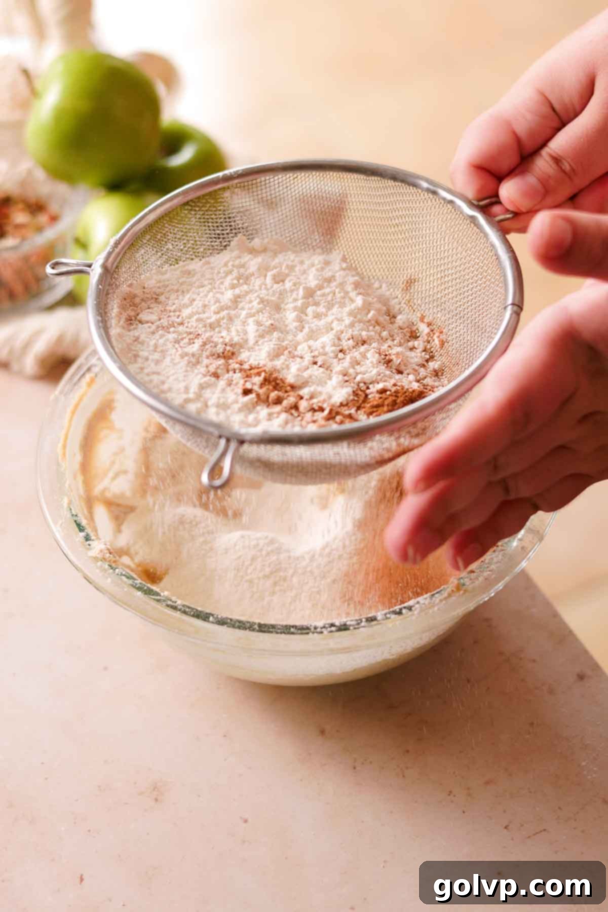 Sifting all-purpose flour, baking powder, and cinnamon directly into the large glass bowl with the creamed butter and sugar mixture.