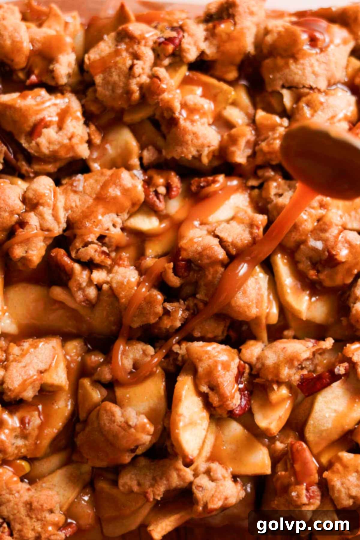 Generously drizzling warm salted caramel sauce over freshly baked apple crumble bars, enhancing their rich flavor.