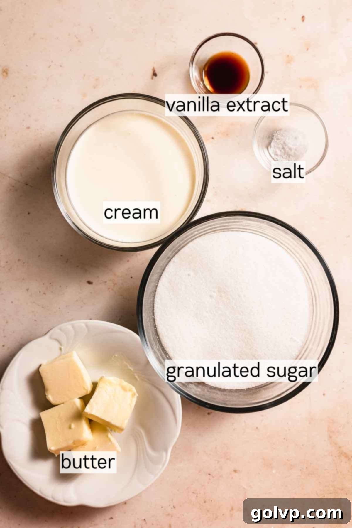 Ingredients for homemade salted caramel sauce, including butter, heavy cream, vanilla extract, sea salt, and granulated sugar.