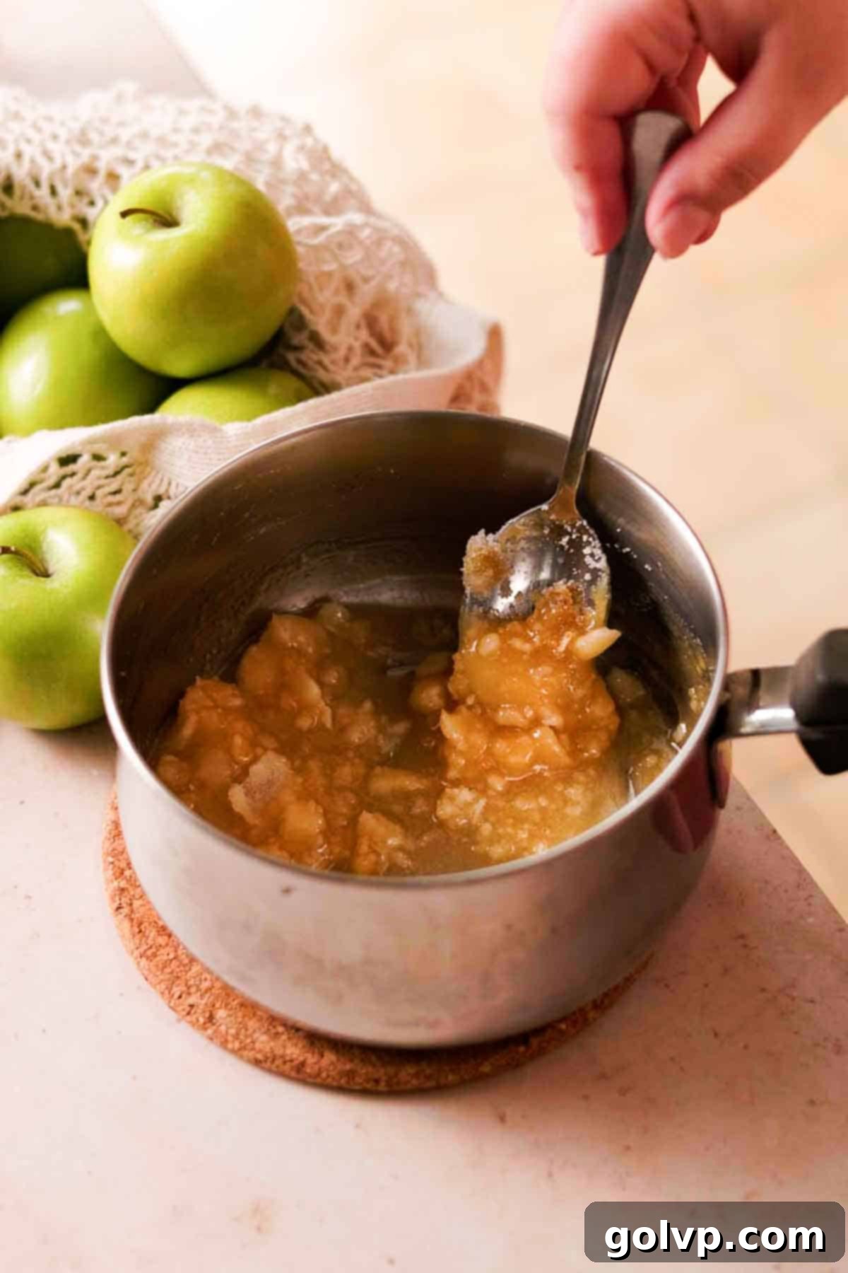 Stirring clumped, partially caramelized granulated sugar in a heavy-bottomed saucepan with a metal spoon.