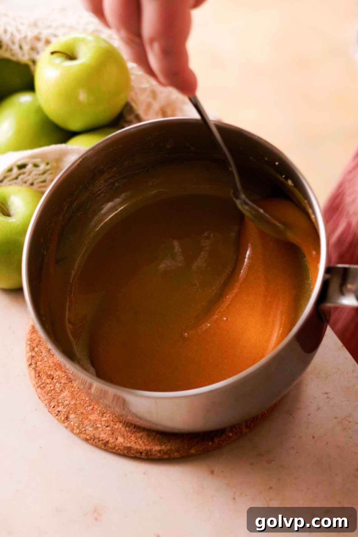 Thick, golden-brown caramelized sugar in a pot, stirred smoothly with a spoon, indicating readiness for cream.