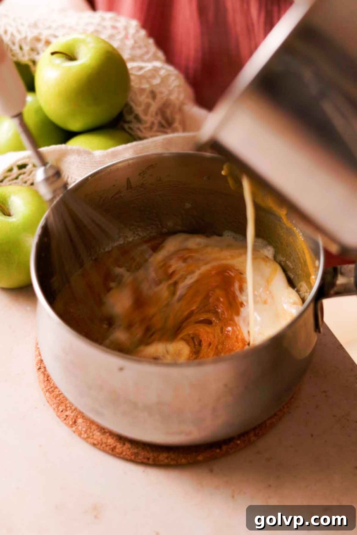 Vigorously whisking hot cream mixture into the hot, caramelized sugar in a pot, creating a smooth caramel sauce.