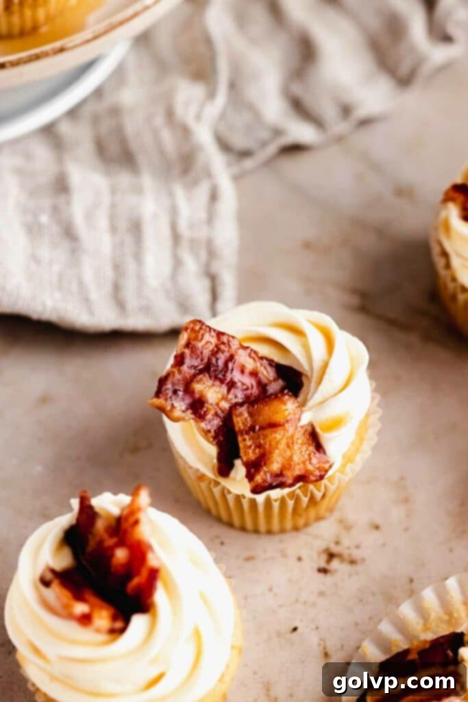 A finished maple bacon cupcake, beautifully frosted with cream cheese and topped with a piece of candied bacon, artfully presented.