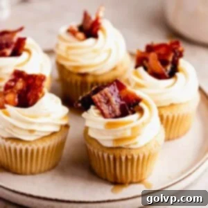 A plate featuring a beautifully frosted Maple Bacon Cupcake, with maple drizzle and candied bacon bits, next to a second cupcake.