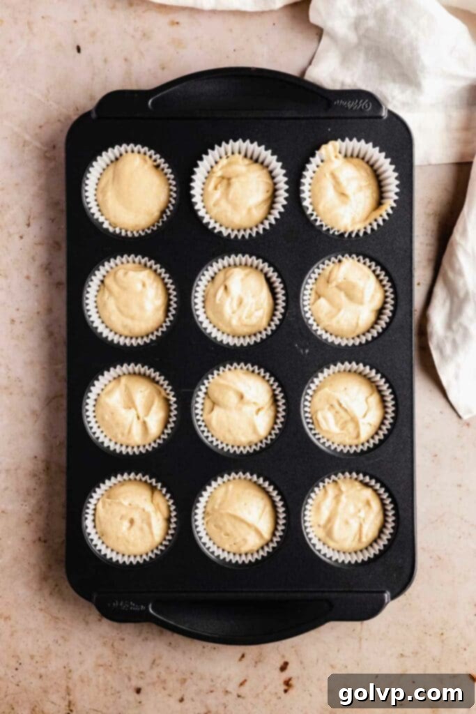 Maple cupcake batter scooped into a cupcake tin lined with paper wrappers, ready for baking.