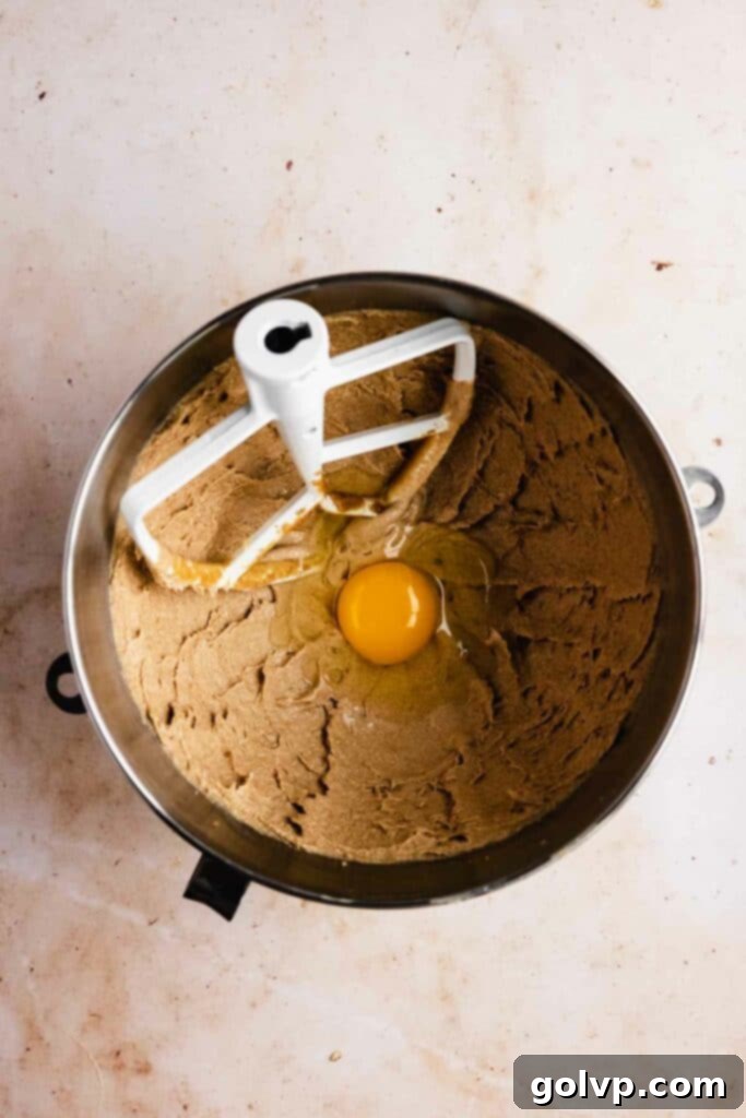 Adding eggs one by one to the creamy butter and oil mixture