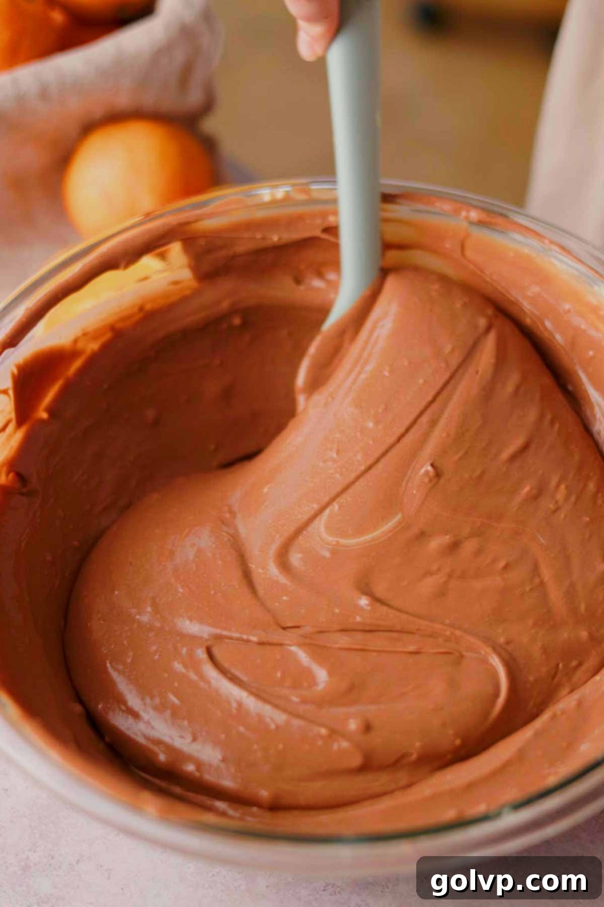 folding chocolate orange cheesecake batter in a glass bowl with a rubber spatula