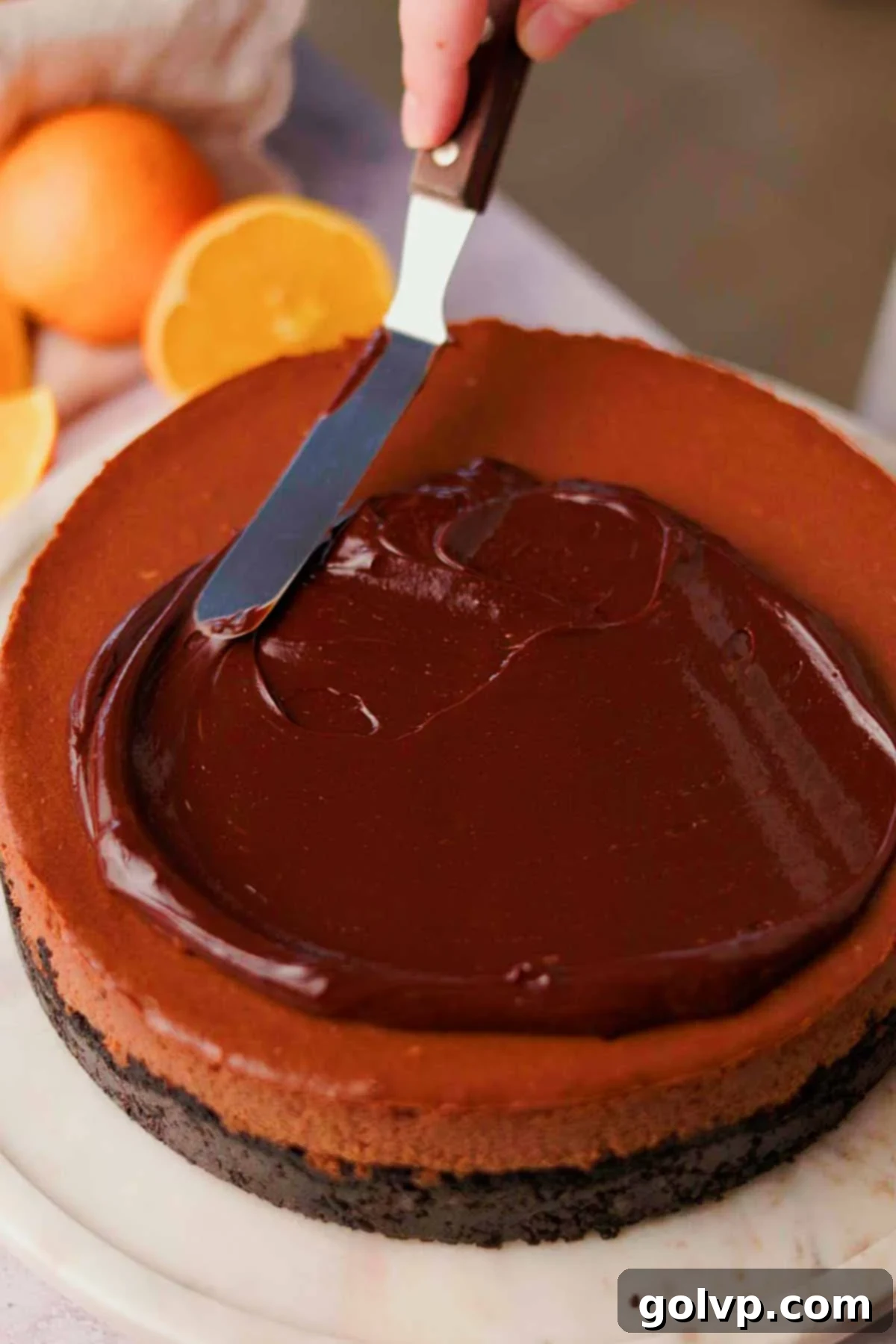 spreading chocolate ganache onto cheesecake with an offset spatula