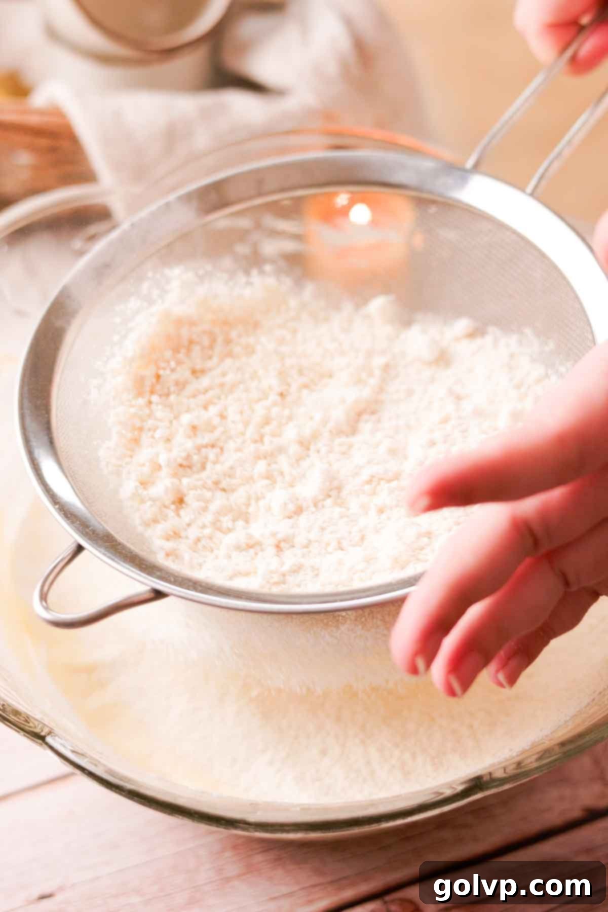 Sifting all-purpose flour into the cake batter with a wire sieve to prevent lumps and ensure a smooth texture.