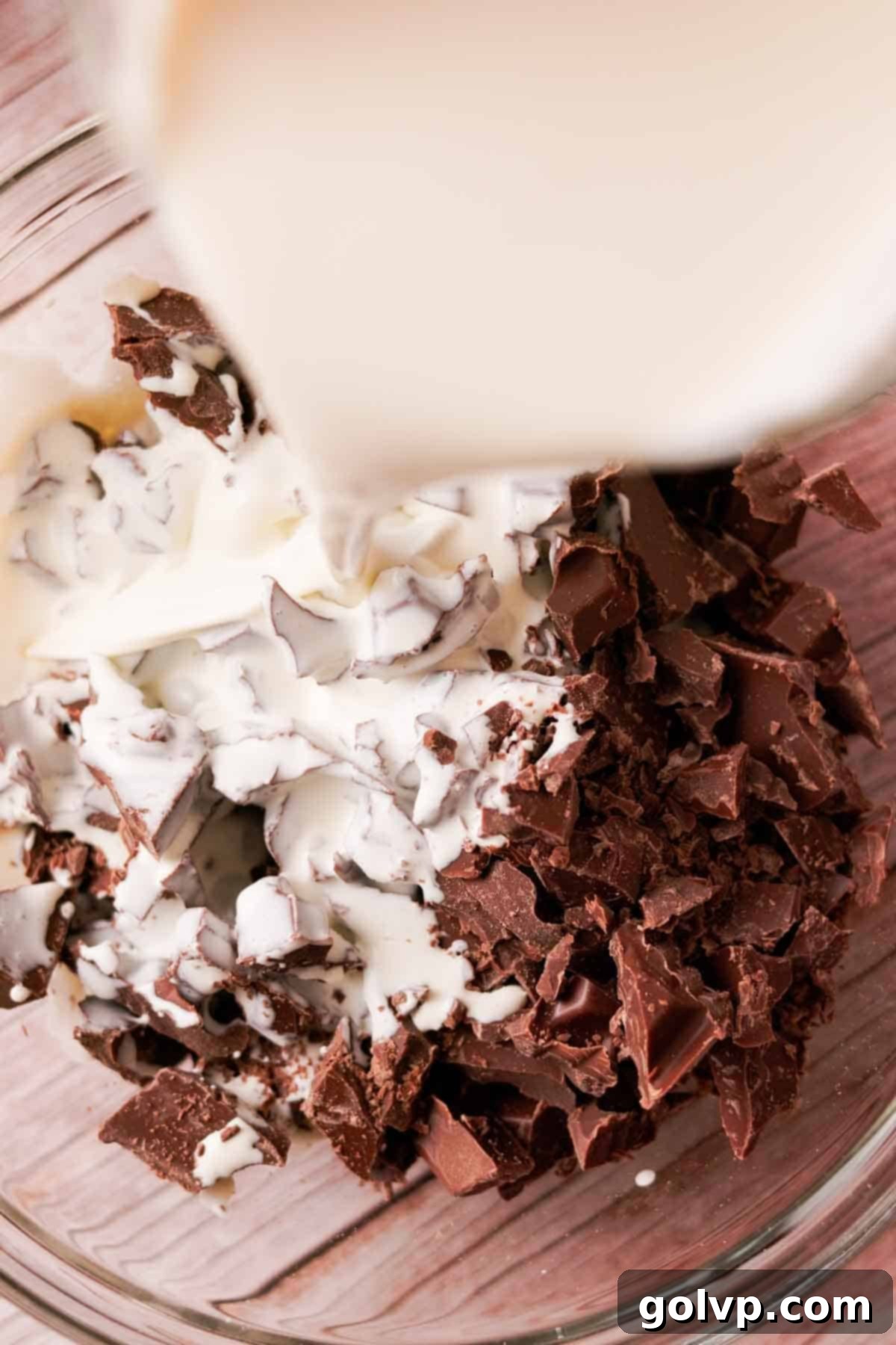 Pour hot heavy cream over finely chopped milk chocolate in a large mixing bowl, preparing to make a smooth ganache.