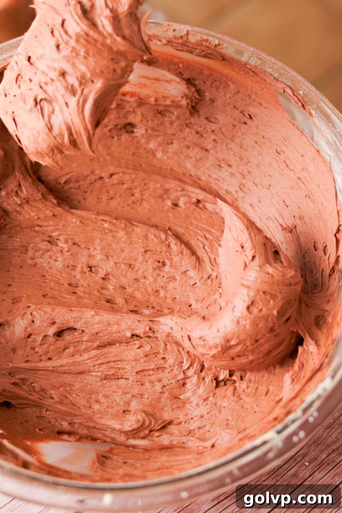 Folding creamy chocolate frosting with a spatula in a mixing bowl, ensuring all ingredients are well combined and smooth.