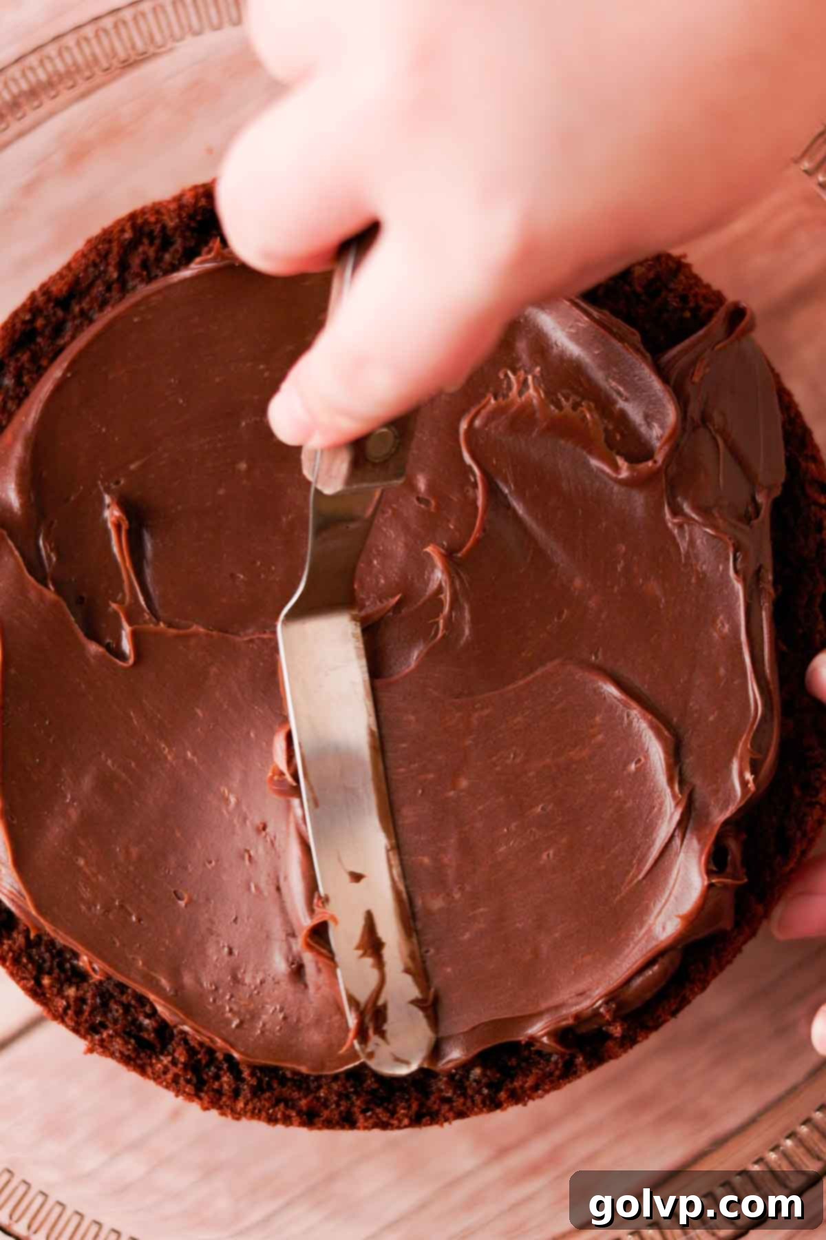 Spreading a generous layer of thickened milk chocolate ganache evenly onto a chocolate cake layer using an offset spatula.